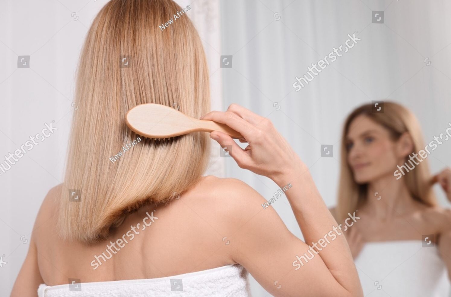 stock-photo-woman-brushing-her-hair-near-mirror-in-room-back-view-2371050487